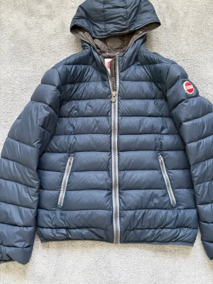 Mörkblå dunjacka från Colmar - Snygg mörkblå dunjacka från Colmar med huva och två dragkedjeförsedda fickor framtill. Jackan är i bra skick och förutom en defekt (se bild 3) Den är i storlek 48 (M) men sitter inte speciellt stort i storleken och jag skulle säga att den passar alla från 170-180. En väldigt stilren och skön jacka för Våren nu. Colmar jackor har ett nypris på ca 5000kr men mitt pris är endast 899kr!!  Tveka ej på att skriva vid minsta fundering eller fler bilder!🤩📦