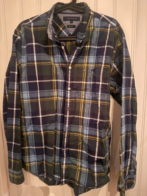 Rutig skjorta Tommy Hilfiger XL - Snygg rutig skjorta från Tommy Hilfiger i blå, grön och gul färg. Skjortan har klassisk krage, knappar framtill och lång ärm. Regular fit-modell som passar perfekt till jeans eller chinos. Ikonisk liten logga på bröstet.