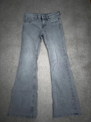 Grå bootcut jeans med låg midja. - Säljer ett par grå jeans med bootcut-modell och låg midja. Klassisk femficksdesign och bälteshällor. Jeansen har en snygg tvättad look och är tillverkade i ett mjukt denimtyg som ger en skön passform.