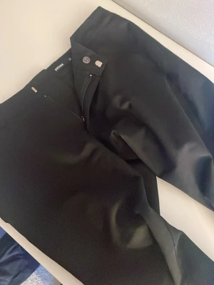 Svarta kostymbyxor från BikBok - Stilrena svarta kostymbyxor från BikBok med rak passform och klassisk midja. Byxorna har knapp- och dragkedjestängning samt släta ben utan synliga fickor. Perfekta för en clean och modern look.