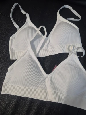 Vita ribbade bhar från H&M - Två vita, ribbade bhar från H&M med smala axelband och mjuk, stretchig känsla. De har en enkel, sömlös design utan bygel och är tillverkade i ett bekvämt material som formar sig efter kroppen. Perfekta för en avslappnad och stilren look.