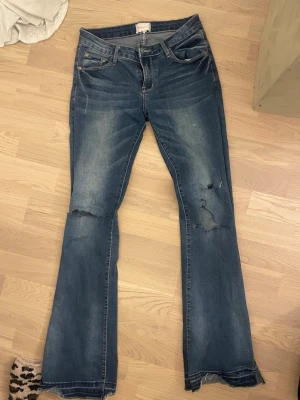 Lågmidjade bootcut jeans - Säljer ett par blå bootcut jeans från Office London med slitningar och hål på knäna. Jeansen har klassisk femficksdesign, låg midja. Passar 36/38
