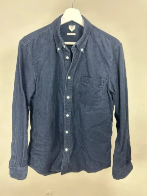 Arket Skjorta i Manchester | M - Stilren mörkblå manchesterskjorta från Arket i mjuk bomull. Klassisk button-down krage, bröstficka och vita knappar framtill. Perfekt för en avslappnad men snygg look. Långärmad och normal passform.