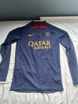 PSG träningströja Nike blå - Mörkblå långärmad träningströja från Nike för PSG med gul logga och Qatar Airways-tryck på bröstet. perfekt för fotbollsträning eller vardags plagg. Nypris 1000kr andvänd 3 ggr ungefär. Inga defekter, hör av er vid funderingar!✌🏼