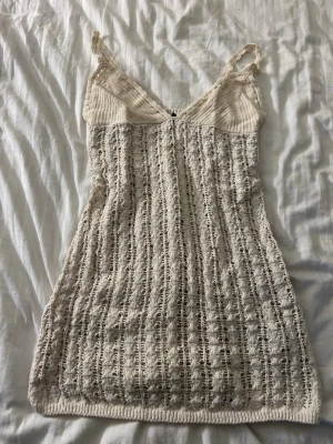 Beige stickad kortklänning H&M - Säljer en beige stickad kortklänning från H&M med smala axelband och v-ringad hals. Klänningen har ett hålmönster och är gjord i ett mjukt stickat material som känns luftigt och somrigt. Perfekt för varma dagar och enkel att styla med accessoarer.