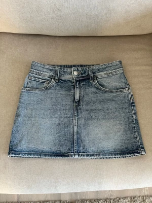 Blå jeanskjol - Säljer en klassisk blå jeanskjol med fem fickor och knappgylf. Kjolen har en lätt utsvängd form. Skriv för mått