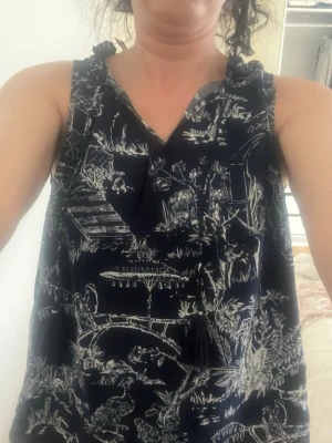 Mörkblå mönstrad ärmlös linnetopp - Snygg mörkblå ärmlös linnetopp med vitt grafiskt mönster och dekorativa tofsar vid halsringningen. Perfekt för en avslappnad och trendig look. Luftig passform och mjukt material.