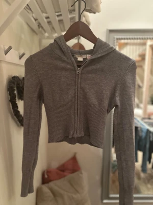 Grå cropped hoodie med dragkedja - Snygg grå cropped hoodie med dragkedja framtill och ribbad midja. Hoodien har långa ärmar och en klassisk huva. Materialet är stickat och känns mjukt och bekvämt. Perfekt för en avslappnad och trendig look. Köpare står för frakt. Skriv vid frågor eller intresse💗