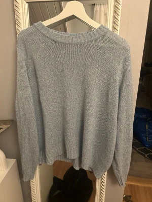 Ljusblå stickad tröja med rund hals - Mysig ljusblå stickad tröja med rundad halsringning och långa ärmar. Tröjan har en enkel, klassisk design med ribbade muddar vid halsen och nederkant. Perfekt att slänga på sig när det är lite kyligt ute.