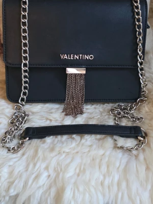 Valentino - Snygg svart axelväska från Valentino i fint skick. Väskan har en stilren, fyrkantig form och är gjord i ett slätt konstläder. Perfekt accessoar för att lyfta din outfit.