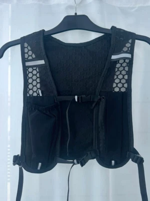 Svart löparväst med mesh och fickor - Säljer en svart löparväst som är mycket lätt och andas bra. Västen har flera fickor framtill och baktill, justerbara remmar och lätt material som passar perfekt för löpning eller trail. Sitter tajt och smidigt på kroppen.