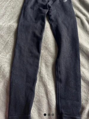 Svarta tights från Gymshark - Säljer ett par svarta tights från Gymshark med deras ikoniska logga på höften. Storlek xs sitter som xxs Tightsen är tillverkade i ett stretchigt och bekvämt material som passar perfekt för träning och sport. De har en ribbad midja och smal passform som framhäver benen.