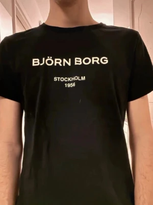 Björn Borg t-shirt - Snygg t-shirt från Björn Borg med vit text på bröstet där det står 'BJÖRN BORG STOCKHOLM 1956'. Klassisk passform och rund hals. Perfekt till jeans eller shorts för en clean och enkel stil.