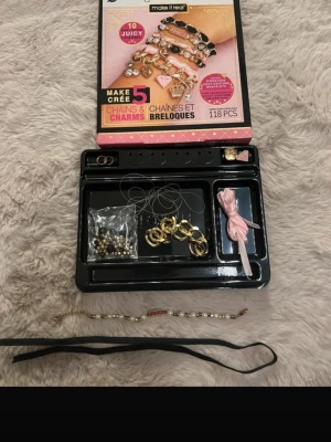 Juicy Couture pärlarmbandskit - Säljer ett Juicy Couture DIY armbandskit med guldfärgade detaljer, vita pärlor och rosa inslag. Kitet innehåller flera kedjor, berlocker och pärlor samt band och tråd för att skapa egna armband. Perfekt för dig som vill designa personliga smycken.