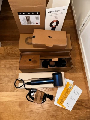 Dyson Supersonic Hairdryer - Säljer en helt ny och oanvänd Dyson Supersonic i färgen Prussian Blue/Rich Copper. Min moster fick denna i bröllopspresent men då hon fick en liknande i en annan färg väljer hon att sälja den vidare då den inte går att lämna tillbaka!  Hårfönen är helt orörd och har aldrig använts. Detta är alltså ett perfekt tillfälle att få tag i en av marknadens absolut bästa hårfönar i fabriksny till bästa pris!!!  (Orginalförpackning, bruksanvisning, stylingtillbehör samt användarhandbok medföljer)