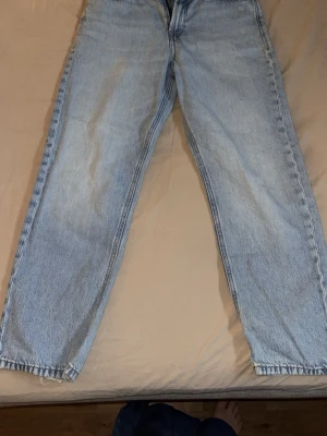 Ljusblå raka jeans från Jack & Jones - Säljer ett par ljusblå jeans från Jack & Jones med rak passform och klassisk femficksdesign. Jeansen är tillverkade i denim och har en snygg vintagekänsla med ljus tvätt. Perfekta för en avslappnad och trendig stil. Dock sliten logga.