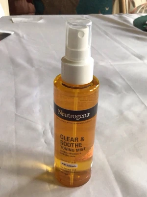 Neutrogena Clear & Soothe Toning Mist - Fräsch ansiktstoner från Neutrogena i sprayflaska, 125 ml. Tonern är gul och innehåller gurkmeja, perfekt för normal och känslig hud. Flaskan är gjord av plast och har en vit spraypump för enkel applicering.