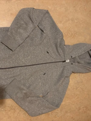 Grå zip hoodie  - Snygg gråmelerad hoodie med dragkedja framtill och justerbar dragsko i huvan. Klassisk modell med ribbade muddar vid ärmslut och nederkant. Perfekt för en chill och avslappnad stil. Materialet känns mjukt och bekvämt. Priset kan diskuteras 
