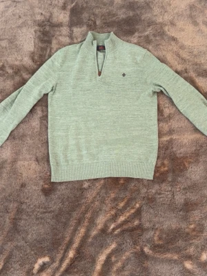 Ljusgrön stickad tröja Morris - Snygg ljusgrön stickad tröja från Morris med halv dragkedja och liten logga på bröstet. Tröjan har ribbade muddar vid ärmslut och nederkant samt en hög krage. Perfekt för lager på lager och stilren look.