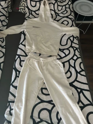 Beige mjukisset med hoodie och byxor - Säljer ett beige loungewear-set med croppad hoodie och matchande mjukisbyxor. Hoodien har tryck på bröstet och byxorna har resår i midjan samt fickor. Perfekt för chill dagar hemma eller när du vill vara bekväm.