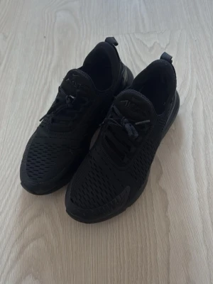 Nike Air Max 270 helsvarta sneakers - Säljer ett par helsvarta Nike Air Max 270 sneakers med mesh-ovandel och synlig Air-enhet i hälen. Skorna har en sportig look med diskreta detaljer och klassisk Nike-logga på sidan. Perfekta för dig som gillar stilrena och bekväma sneakers.