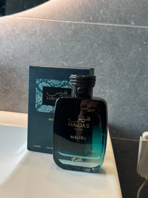 Hawas for Him Malibu parfym - Snygg parfymflaska från Hawas, modellen Malibu. Flaskan är i glas med en mörkblå till turkos färgskiftning och har ett elegant svart lock med detaljer. Kommer i matchande förpackning med stilren design.