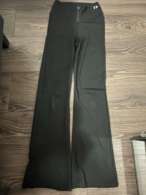 Svarta bootcut leggings lager 157 - Snygga svarta leggings från lager 157 med bootcut-modell och hög midja. De har en liten dragkedja framtill och är tillverkade i ett stretchigt material som sitter bekvämt. Perfekta för en trendig och avslappnad look. Byxorna är i storlek M.