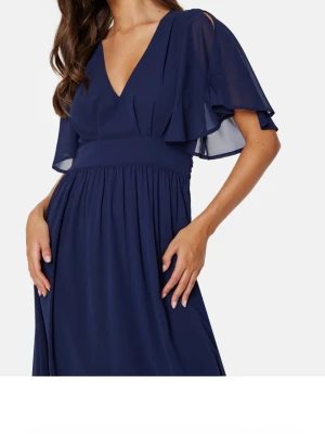 Marinblå långklänning med v-ringning - Elegant marinblå långklänning med djup v-ringning och luftiga, korta ärmar med slits. Klänningen har markerad midja och ett mjukt, fallande tyg som ger en fin siluett. Perfekt för speciella tillfällen.