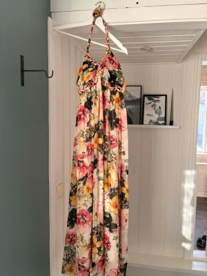 Blommig långklänning från Rut m.fl. - Säljer en blommig långklänning från Rut m.fl. i storlek 34. Klänningen har halterneck med flätade band och ett färgstarkt blommönster i rosa, gul, grön och svart på ljus botten. Perfekt för sommarens alla tillfällen!