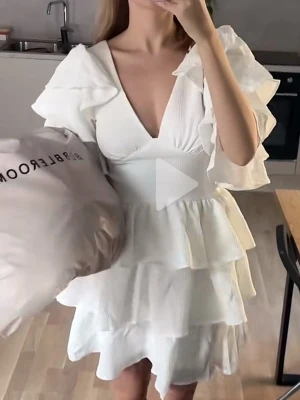 Vit volangklänning med v-ringning - Supersöt vit klänning med djup v-ringning och flera lager volanger. Klänningen har korta, vida ärmar och markerad midja som ger en feminin siluett. Perfekt för sommarens alla tillfällen och ger en romantisk vibe.