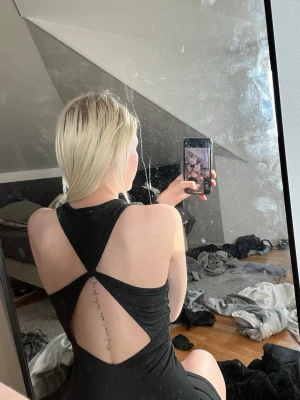 Svart tight kortklänning - Säljer en svart, tight kortklänning med snygg öppen rygg och korsade band. Klänningen har en enkel, stilren framsida och är ärmlös med rund halsringning. Perfekt för dig som gillar minimalistisk och trendig stil.