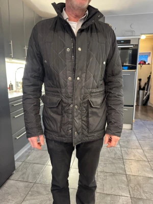 Hugo Boss jacka - Snygg svart quiltad jacka från Hugo Boss med hög krage och tryckknappar. Jackan har två stora framfickor och dragkedja framtill. Passar perfekt till vardagslooken och har en klassisk, stilren design. Kan gå ner i pris vid snabb affär. Kan mötas upp i Stockholm