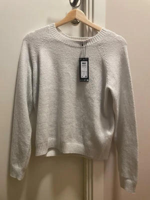 Vit stickad tröja från Gina Tricot - Klassisk vit stickad tröja från Gina Tricot med rund halsringning och ribbade muddar vid ärmslut och nederkant. Tröjan har en enkel och stilren design som passar till det mesta. Materialet ser mjukt och bekvämt ut, perfekt för kyligare dagar.