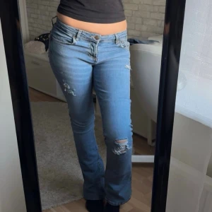Blå bootcut jeans med slitningar - Snygga blå bootcut jeans med slitningar på låret och knät, hålen har jag gjort själv! Midjemått: 37cm rakt över, Innerbenslängd: 79cm.