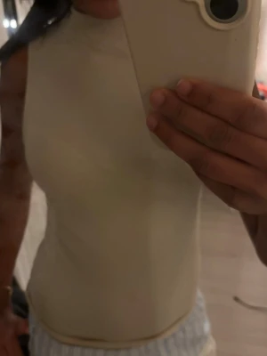 Beige ribbad ärmlös topp - Säljer en beige, tight och ribbad ärmlös topp med rund hals. Toppen har en enkel och stilren design som passar perfekt till jeans eller kjol. Materialet känns mjukt och stretchigt för en bekväm passform.