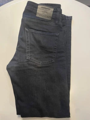 Jeans från Jack & Jones - Snygga svarta jeans från Jack & Jones med klassisk femficksdesign och rak passform. Jeansen har en diskret tvätt och är tillverkade i mjukt denimtyg som ger en bekväm känsla. Perfekta för en avslappnad och stilren look. Storlek 30/32!