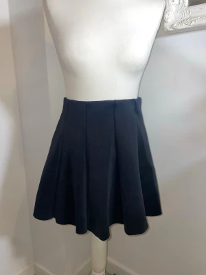 Svart kortkjol med vidd - En svart kortkjol med utsvängd passform och mjukt fall. Kjolen har en enkel, stilren design utan synliga detaljer och passar perfekt till många olika looks. Tillverkad i ett bekvämt material som ger en snygg siluett.