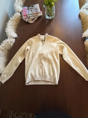 Beige stickad tröja (Jack & Jones) - Snygg beige stickad tröja med v-ringad hals och ribbade muddar. Tröjan har lång ärm och är tillverkad i ett mjukt, tunt material som passar perfekt till lager-på-lager. Enkel och stilren design utan synliga loggor.