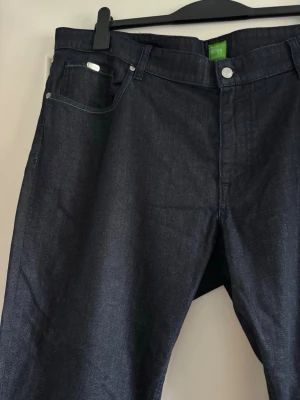 Mörkblå jeans från Hugo Boss - Snygga mörkblå jeans från Hugo Boss i klassisk rak modell. Jeansen har silverfärgade detaljer och dragkedja i gylfen. Tillverkade i slitstark denim som ger en stilren look. Perfekta för dig som gillar tidlös och enkel stil.