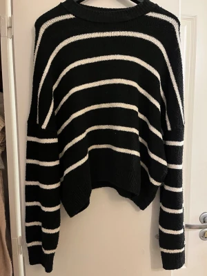 Svartvit randig stickad tröja NA-KD - Säljer en svart stickad tröja från NA-KD med vita horisontella ränder. Tröjan har avslappnad passform, rund halsringning och ribbade muddar. Perfekt för lager på lager och enkel att styla till olika outfits.