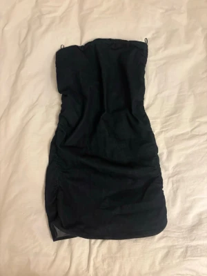 Svart axelbandslös kort klänning - Säljer en svart kort bandeu klänning i jeans/ denim material. Klänningen har rynkade sidor som ger en snygg siluett och är perfekt för dig som gillar en stilren och enkel look. Passar till många olika tillfällen och är lätt att matcha med accessoarer. Från Zara i storlek xs, aldrig använd💞✨