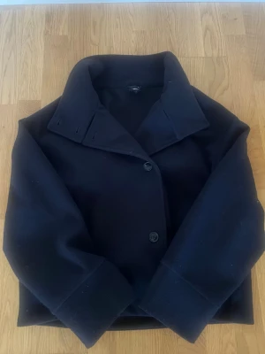 Marinblå ullkappa Gina Tricot  - Stilren mörk marinblå kappa,tillverkad i ett tjockare ullmaterial som håller värmen. Perfekt för kyliga dagar och enkel att matcha med olika outfits. Använd 1gång köpt från Gina Tricot 