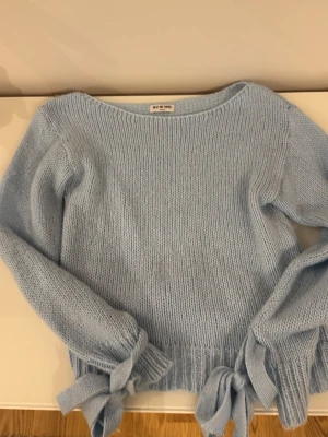 Ljusblå stickad tröja med knyt från meet me there  - Supersöt ljusblå stickad tröja från meet me there  med rund halsringning och långa ärmar. Tröjan har ribbade muddar och snygga knytband vid ärmsluten som ger en extra detalj. Perfekt för dig som gillar en mjuk och trendig look.