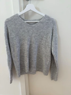 Ljusgrå stickad tröja från ONLY - Mysig ljusgrå stickad tröja från ONLY med v-ringning och ribbad struktur. Tröjan har långa ärmar och en avslappnad passform, perfekt för lager på lager. Enkel och stilren design som passar till det mesta. Det står XS men den är mer som en S/M. 