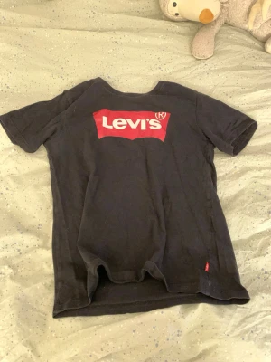 Svart Levi's t-shirt med logga - Säljer en svart t-shirt från Levi's med den klassiska röda loggan framtill. T-shirten har korta ärmar och rund halsringning. Perfekt för dig som gillar enkel och stilren streetwear.