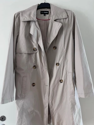 Beige trenchcoat från Kappahl  - Beige trenchcoat från Kappahl med dubbelknäppning, klassisk krage och bälte i midjan. Jackan har två sidofickor, dekorativa knappar och ett sprund bak. Snyggt till våren/ hösten. Kan diskutera pris men Orginal ca 500kr och aldrig använd💕