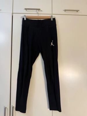 Svarta leggings från Jordan - Säljer ett par svarta leggings från Jordan med den klassiska Jumpman-loggan på låret. De har hög midja och är tillverkade i ett mjukt och stretchigt material som passar perfekt till träning eller chill. Supersnygga och bekväma!