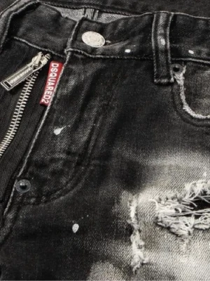 Svarta slitna jeans från Dsquared2 - Säljer ett par svarta jeans från Dsquared2 med slitningar, blekta detaljer och dragkedja framtill. Jeansen har en cool, tvättad look och tydliga distressed-effekter. Materialet är klassisk denim och det finns en röd Dsquared2-tag vid fickan.  Prisetkan sänkas vid snabbaffär.