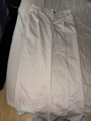 Vida beige kostymbyxor Gina Tricot - Säljer ett par snygga beige kostymbyxor från Gina Tricot. Byxorna har hög midja, vida ben och pressveck framtill för en clean look. Tillverkade i ett mjukt tyg som känns skönt mot huden. Perfekta för dig som gillar stilrena och trendiga outfits., Storlek S