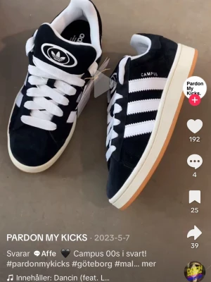 Adidas Campus 00s svart/vit sneaker - Snygga Adidas Campus 00s sneakers i svart mocka med vita detaljer och klassiska tre ränder på sidan. Skon har vit sula med gummiyttersula och vita skosnören. Tydlig Adidas-logga på plösen och texten CAMPUS på sidan.